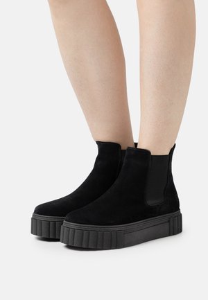 Bottines en daim noir avec des panneaux élastiques sur les côtés et une semelle en caoutchouc épaisse et striée. Texture lisse avec un design minimaliste.