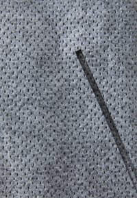 Grå perforerad tyg med små hål och diagonalskärning, som visar en texturerad yta med en slät finish.