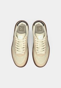 Par de zapatillas beige Veja con punteras perforadas, cordones crema y suelas marrones vistas desde arriba sobre fondo blanco.