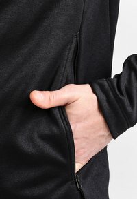 Zwarte zip-up jack met een gladde textuur, aansluitend ontwerp en een voorkennis met een hand erin.