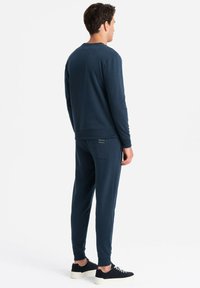 Sudadera color azul marino y joggers a juego en tejido suave, con puños acanalados y un sutil detalle de etiqueta en el bolsillo trasero.