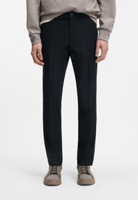 Μαύρο παντελόνι με εφαρμογή κοψίματος, με κουμπωτό κλείσιμο, πιέτες στο μπροστινό μέρος και ομαλή υφή υφάσματος, συνδυασμένο με γκρι αθλητικά παπούτσια.