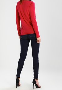 Rosa langärmliges Oberteil, eng anliegend aus weichem Material, kombiniert mit dunklen Denim-Jeans. Schwarze High Heels runden das Outfit ab.