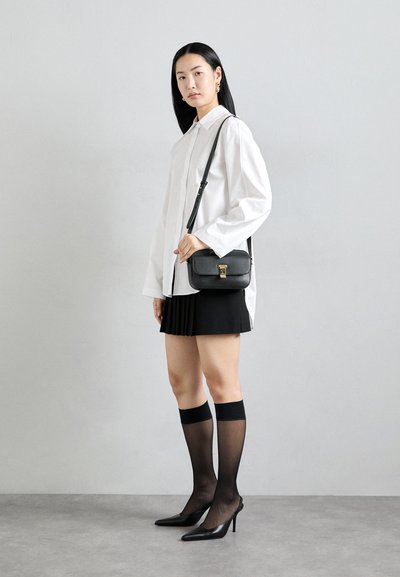 Svart axelväska med texturerad yta, guldinfattningar och justerbar rem, tillsammans med en vit skjorta och svart plisserad kjol.