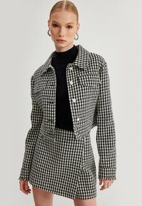 Zwart-witte houndstooth jas met een cropped fit en parelknoopjes, gecombineerd met een bijpassende rok met een zij-split.
