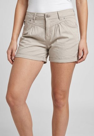 Woman wearing beige cuffed shorts and a white top, showing front view from waist to mid-thigh.
