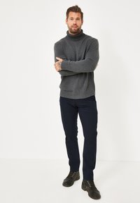 Grauer Strickpullover mit Rollkragen und geripptem Saum, kombiniert mit marineblauen Slim-Fit-Hosen. Modell trägt schwarze Schnürstiefel. Schlichter weißer Hintergrund.