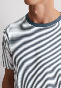T-shirt rayé en coton, avec de fines rayures bleu marine et blanches, un col rond bleu marine et des manches courtes. Texture douce avec un design décontracté.