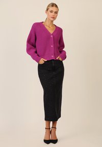 Fuchsia gebreide cardigan met een V-hals, voorzien van grote knopen aan de voorkant. Gepaard met een zwarte denim rok versierd met kleine witte stippen.