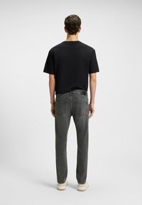 T-shirt nera con colletto a giro, abbinata a jeans in denim grigi con due tasche posteriori e cuciture chiare. Calzature beige con finitura testurizzata.