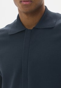 Marinblå stickad polo tröja med en mjuk textur, utrustad med en vikbar krage och design med dold knäppning, som visar enkla, rena linjer.