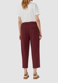 Bordeaux op maat gemaakte broek met een rekbare tailleband, verkorte lengte en twee achterzakken, gecombineerd met een witte overhemd met korte mouwen en casual schoenen.