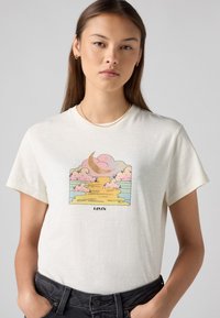 Krémové bavlněné tričko s pastelovou grafikou znázorňující srpek měsíce, oblaka a západ slunce nad vodou. Logo text pod designem. Krátké rukávy.