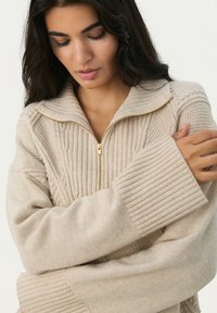 Beige knitted pullover with a high collar, half-zip front, ribbed cuffs, and intricate texture patterns on the fabric.