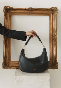 Sac à main en cuir noir avec une finition texturée, forme incurvée, bandoulière tressée, accents en matériel doré et fermeture à glissière visible.