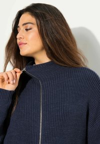 Mörkblå zip-up sweater med ribbad textur, hög krage och silverfärgad dragkedjedetalj, med en figurvänlig silhuett och avslappnad passform.