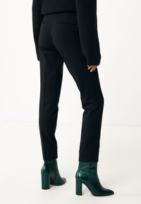 Pantalones negros de corte entallado con un ajuste slim, que cuentan con bolsillos traseros y un ligero dobladillo. Combinados con botas de tobillo brillantes verdes con tacones de bloque.