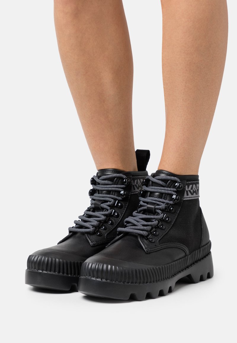 Μαύρες μποτάκια μέχρι τον αστράγαλο με υφή, στρογγυλή μύτη, χοντρή καουτσούκ σόλα, γκρίζες κορδόνες με μεταλλικές θηλιές, κολάρο με σήμα και λαβή.