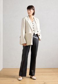 Blazer beige à rayures avec des manches larges, boutons noirs, un gilet assorti, un pantalon en cuir noir et un sac crème texturé. Chaussures dans des tons neutres.