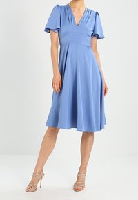 Lichtblauwe jurk tot de knie met korte vlindermouwen, een diepe V-hals en paneel-details op het lijfje. Glad materiaal, A-lijn silhouet.