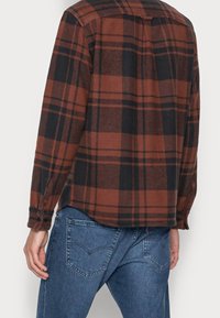 Červená a černá kostkovaná flanelová košile s dlouhými rukávy, s knoflíkovým zapínáním a uvolněným střihem, v kombinaci s modrými džíny.