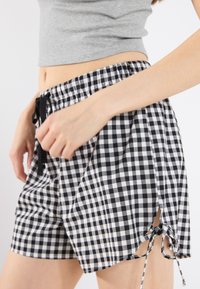 Black and white gingham shorts with an elastic waistband and drawstring. Features side slits with ties for adjustable fit.