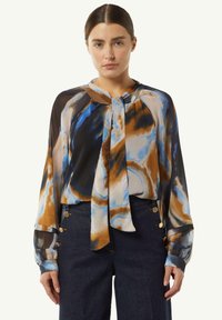 Bunt gemusterte Bluse mit blauen, braunen und cremefarbenen abstrakten Mustern. Lange Ärmel mit Manschetten; Bänder am Hals. Leichter, fließender Stoff.