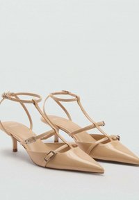 Nude lakirane slingback pete s šiljastimi nosovi, trakovi za gležnje in malimi blokastimi petami; vsebuje srebrne zaponke.