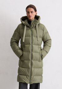 Gewatteerde jas met capuchon in olijfgroen. Voorzien van een ritssluiting aan de voorkant, twee zijzakken en een effen patroon. Gemaakt van een glad, waterafstotend materiaal.