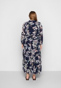 Květinové maxi šaty v námořnické modři s dlouhými rukávy, volánkovým lemem a vypasovaným pasem, s růžovými a modrými květinovými vzory na hladké tkanině.