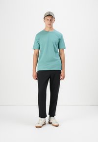 Tricou din bumbac de culoare albastră deschisă asociat cu pantaloni negri și adidași albi. Capac gri cu o textură subtilă. Design curat și minimalist.