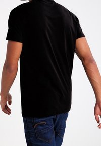 Czarny t-shirt z krótkim rękawem wykonany z gładkiej tkaniny, z zaokrąglonym dekoltem. Widok od tyłu ukazuje prosty design bez widocznych wzorów i ozdób.