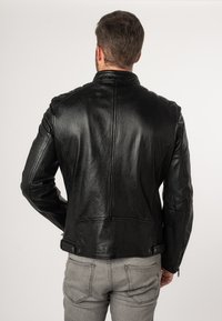Schwarze Leder-Motorradjacke mit körpernahem Design, auffälligen Nähten und Druckknöpfen an der Taille. Glatte Textur mit klassischem Kragen.