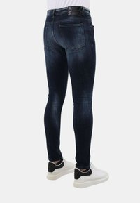 Donkerblauwe slim-fit jeans van denim, met vijf zakken en subtiele vervaging. Gepaard met witte sneakers met zwarte accenten.