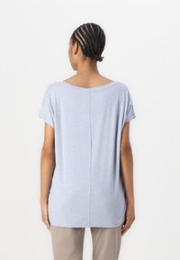 Top azzurro chiaro a maniche corte con scollatura rotonda, tessuto morbido e una cucitura centrale sul retro. Abbinato a pantaloni beige.