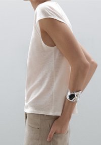 Lys beige, kortærmet skjorte i en blød tekstur med en afslappet pasform. Sølv armbånd med et sort accent. Sidesyn.