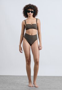 Melna un bēša punktiņu bikini ar bandeau topu un augstām jostasvietām, ar plānām siksnām un teksturētu audumu.