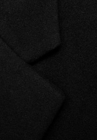 Primer plano de tela de lana negra con capas superpuestas que muestran un material suave y texturizado, así como pliegues sutiles.