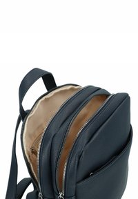 Sac à dos en cuir bleu marine foncé avec plusieurs compartiments zippés et une doublure en tissu beige. Dispose de bretelles réglables et d'une surface texturée.