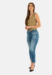 Top sin mangas de color tostado con botones, combinado con unos jeans ajustados de color azul claro y unos zapatos de tacón negro con punta. Diseño sencillo y ajuste casual.