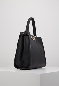 Sac à main texturé noir avec une forme structurée, doté d'une poignée supérieure et d'un détail en métal doré à l'avant.