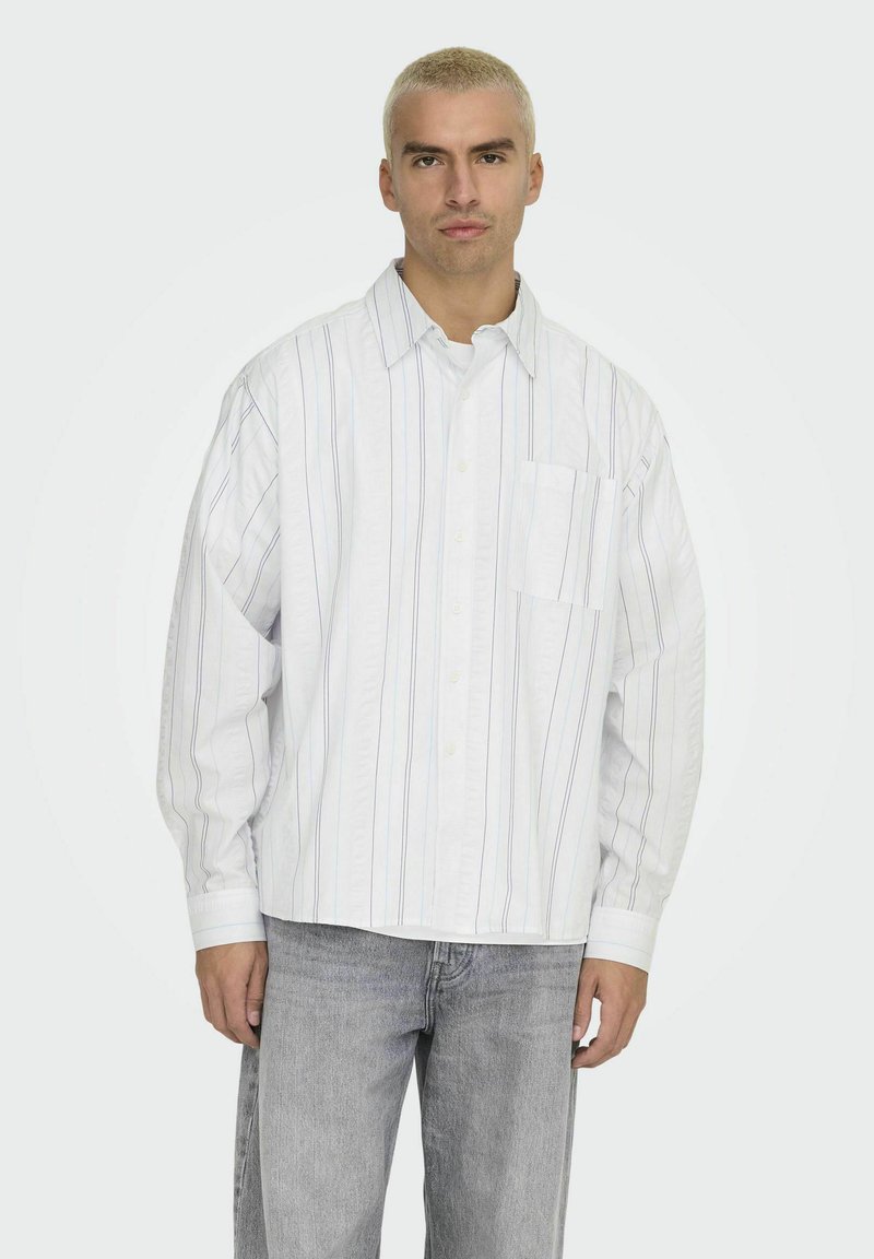 Witte overhemden met blauwe en grijze verticale strepen, met een borstzak en een relaxte pasvorm. Draagt met lichtgrijze jeans.