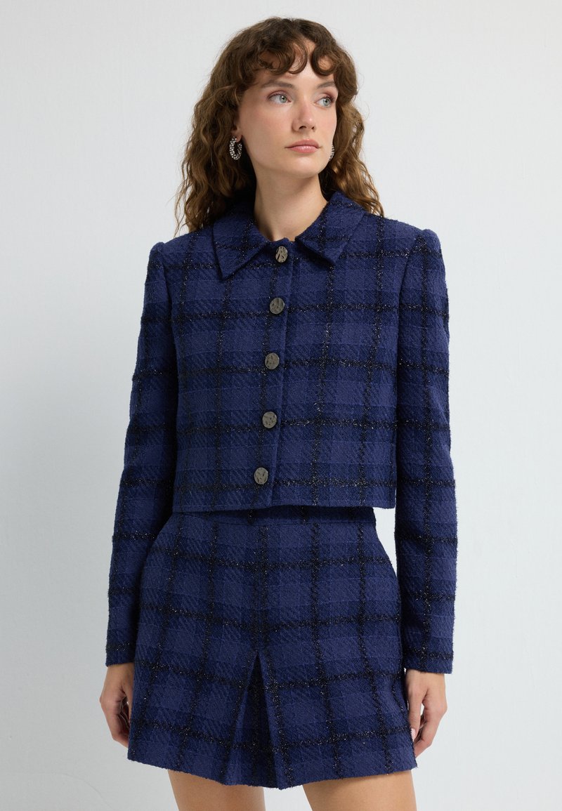 Navyblå tweedjacka med en kortad design, stor krage och sex runda knappar, i kombination med en matchande kjol med en slits fram.