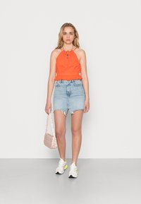 Top laranja com alças e bainha em babado, combinado com uma saia de ganga azul clara de cintura alta. Ténis brancos com detalhes neon e uma bolsa floral.