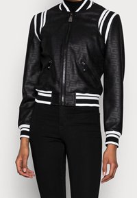 Blouson aviateur noir en cuir avec un motif en relief subtil, col et poignets côtelés avec rayures blanches, et poches latérales zippées.