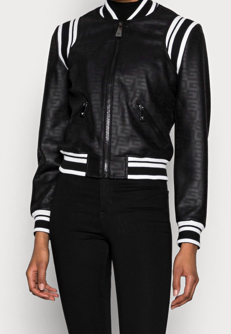 Blouson aviateur noir en cuir avec un motif en relief subtil, col et poignets côtelés avec rayures blanches, et poches latérales zippées.