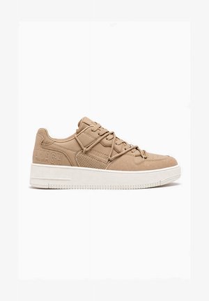 Zapatilla beige de perfil bajo con paneles perforados y de ante, logo en relieve en el lateral, cordones beige, y suela gruesa blanca de goma.