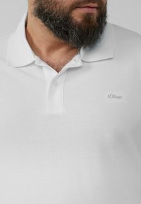 Witte polo met een,textuurstof, klassieke kraag en drie-knopssluiting. Voorzien van een klein, geborduurd s.Oliver-logo op de borst.