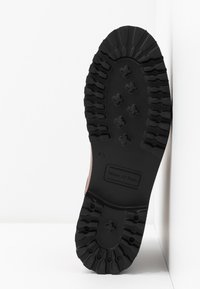 Semelle en caoutchouc noir avec un motif de bande de roulement texturé, featuring des formes hexagonales et le nom de la marque en relief. Vue de côté sur fond blanc.