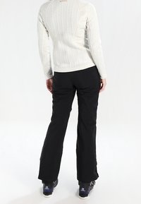 Maglia a maniche lunghe di un beige chiaro testurizzato con scollatura rotonda, abbinata a pantaloni neri slim-fit. Indossata con scarpe basse nero e grigie.